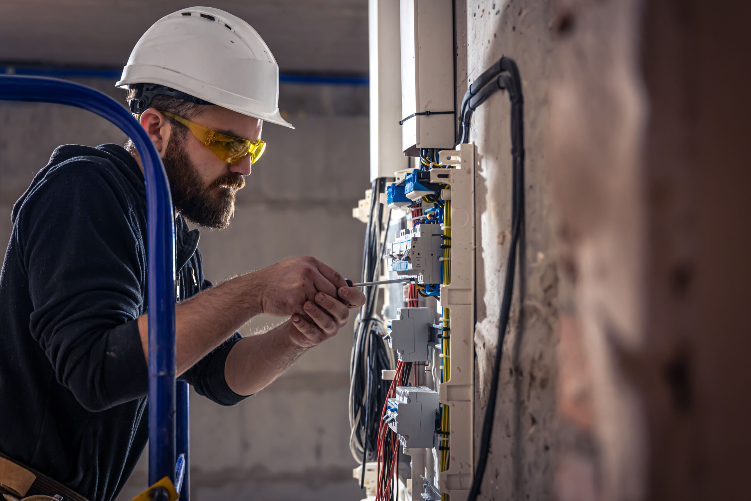 A male electrician works in a switchboard with an electrical connecting cable. - male electrician works switchboard with electrical connecting cable scaled